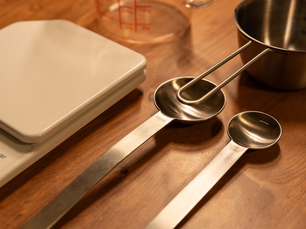 A close-up of kitchen utensils including a scale, measuring cups, and spoons on a wooden counter.